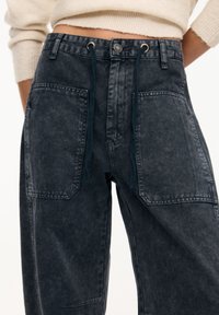 Tumman pesun farkut, joissa on väljä istuvuus, suuret etutaskut, narunauhashenkäri ja metallinen nappisuljin.