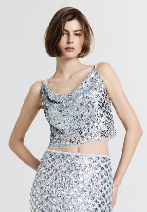 Top corto in paillettes argento con scollatura a cowl, dotato di spalline sottili e superficie texturizzata. Completato da una cintura elastica.