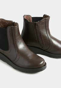 Bruna läderankelboots med elastiska sidopaneler, sidodragkedja och texturerade gummisålar. Har sydda accenter och en mjuk insida.