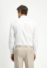 Witte overhemd met lange mouwen, knoopmanchetten en een klassieke kraag, gecombineerd met lichtbeige broek met achterzakken en knopen.