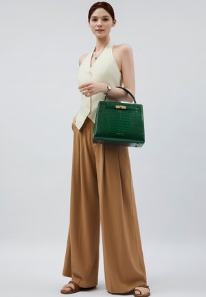 Sac en bandoulière en simili crocodile vert avec un fermoir doré, porté avec un top halter jaune pâle et un pantalon large beige. Texture lisse.
