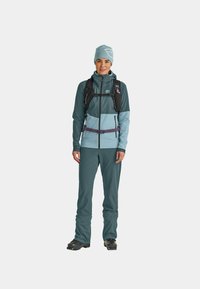 Teal and light blue outdoor outfit, featuring a zip-up jacket with hood and matching pants. Includes a black hydration pack and beanie.