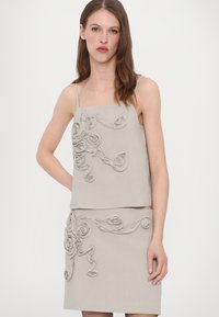 Beige Zweiteiler bestehend aus einem ärmellosen Top und einem Rock, beide verziert mit strukturierten Stoffblumen und wirbelnden Akzenten.