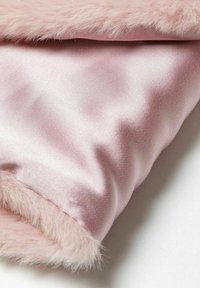 Lyserød kunstpelsstof med en glat satinbagside. Kantene har en blød, fluffy tekstur, der kontrasterer med den glatte overflade.