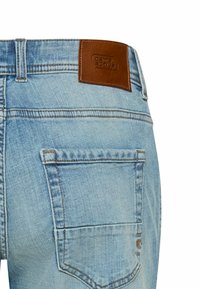 Light blue denim jeans with a brown leather patch at the waistband. Features two back pockets with stitching details and a faded texture.