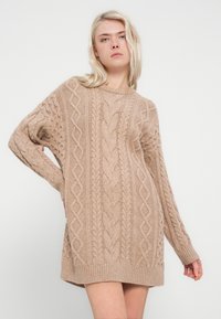 Beige knitted sweater with cable patterns, long sleeves, round neckline, and ribbed hem. Soft texture and oversized fit.