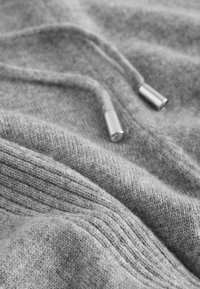 Gray knitted sweatshirt fabric with a soft texture, featuring a drawstring with metallic end caps and ribbed detailing.