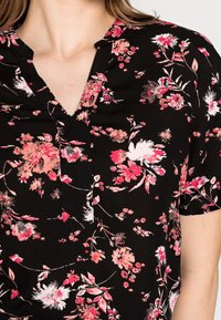 Black floral blouse with short sleeves. Features pink and white flower patterns, v-neckline, and lightweight fabric.