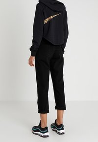 Person som bär svarta korta byxor, svart kort huvtröja med leopardmönster på Nike-logotypen och svarta sneakers med turkosa och lila detaljer.