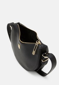 Sac en cuir noir texturé avec une silhouette courbée, fermeture éclair dorée et quincaillerie. Ouvert sur le haut, révélant un intérieur spacieux. Sangle réglable incluse.