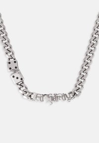 Sølvkjede med to terningformede accenter og en tekstvedheng i en utsmykket skrifttype, som viser en polert metallfinish.