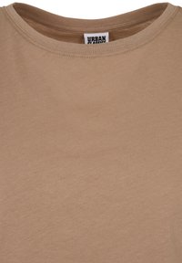 Beige bomulls t-shirt med rund halsringning och korta ärmar. Tyget har en slät textur och minimal sömdetalj.