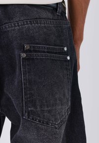 Jeans in denim nero con una finitura testurizzata. Presentano due tasche posteriori con bottoni argentati e una vestibilità dritta. Passante per cintura visibile in vita.