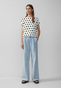 Witte top met zwarte stippen, korte mouwen, gecombineerd met lichtblauwe wijde jeans met zijzakken en een relaxte fit, gedragen met zwarte sandalen.