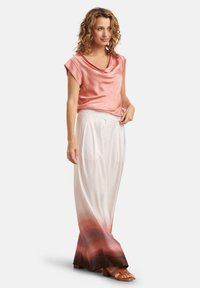 Zachte roze blouse met drapering, gecombineerd met witte broek met wide legs, die een ombre-effect heeft dat overgaat van wit naar donkerbruin aan de zoom.