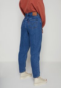 Högmidjade blå denimjeans med lös passform, med två bakfickor och en läderlogotyp på midjebandet.