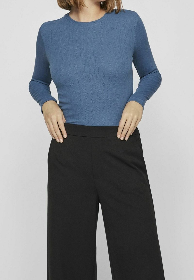 Top azul de manga larga con un patrón texturizado, combinado con pantalones de tiro alto de pierna ancha en negro. Tejido suave y diseño ajustado.