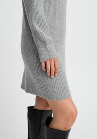 Abito in maglia grigia a coste con maniche lunghe e leggero svaso all'orlo. Il tessuto è testurizzato; indossato con stivali neri alti fino alla coscia.