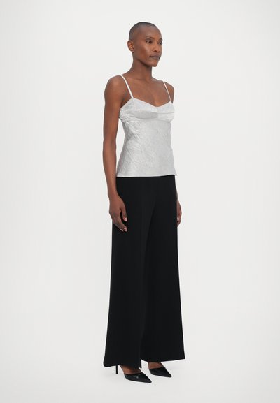 Top de tirantes finos, ligero y ajustado en color plateado; combinado con pantalones anchos negros y tacones de punta negra.