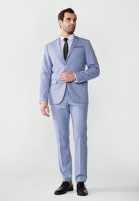 Light blue suit with a single-button jacket, notch lapels, and a matching pair of trousers. White shirt and black tie complete the look.