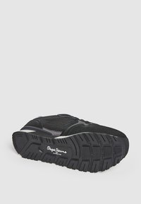 Black athletic shoe featuring a mesh upper, suede accents, and a textured rubber sole with a pronounced tread design. Brand logo visible.