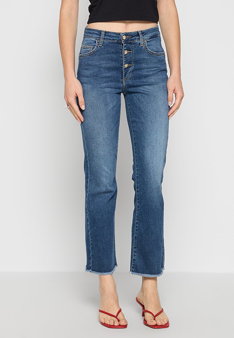 Jeans aus Denim in mittelblau, hoch-tailliert mit einem fünfteiligen Knopfverschluss, Ausbleichungen und rohem Saum. Kombiniert mit roten Flip-Flops.