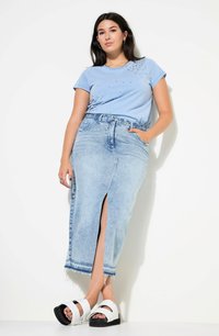 Camiseta de algodón azul claro con tachuelas decorativas plateadas, combinada con una falda de mezclilla desgastada con una abertura frontal y dobladillo sin acabar, complementada con sandalias blancas.