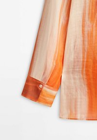 Chemise à manches longues avec un dégradé orange et crème. Comprend un poignet boutonné avec un petit bouton rose, un tissu léger et une texture lisse.