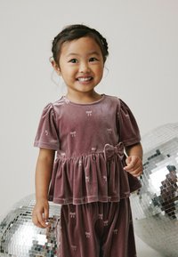 Samt-Zweiteiler in Mauve mit kurzen Puffärmeln, rüschigem Peplum-Oberteil und Schleifendetails, ergänzt durch passende Hosen.