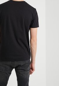 Svart t-shirt med kort ärm, i bomullsmaterial, figurnära design, rundad halsringning, matchad med mörka denimjeans med bakfickor.