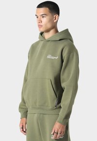 Oliivivihreä huppari, joka on valmistettu puuvillasekoitteesta. Edessä tasku, resorikujat sekä rintapainatus. Sisältää nyörikauluksen.