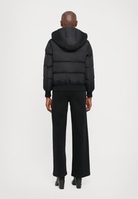 Veste noire rembourrée avec capuche, dotée de sections matelassées, de poignets côtelés et d'un design court. Portée avec un pantalon large noir taille haute.