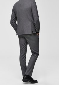 Gray tailored suit with a textured finish and single vent at the back. Paired with black dress shoes. Natural fabric drapes smoothly.