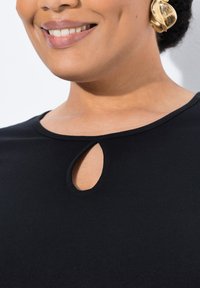 Musta paita, jossa on kaareva pääntie ja pieni avaus. Suora pinta ja tiukka malli korostavat solisluitasi.