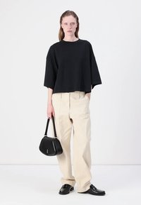 Μαύρο κοντό μπλουζάκι με κοντά μανίκια, συνδυασμένο με κρεμ παντελόνι σε φάρδος, μαύρη τσάντα και μαύρες μοκασίνες, σε ουδέτερο φόντο.