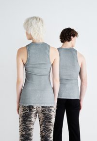 Two individuals stand back-to-back, wearing fitted gray tank tops. Textured fabric with a ribbed pattern; paired with patterned and solid pants.