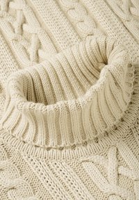 Kreemjooksu värvi kudumiga sviiter, millel on volditud ribitud turtleneck krae ning lõngapinu mustri taust.