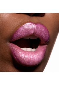 Glansende, metalliske lyserøde læber med tekstureret, iriserende finish, der fremhæver en glat kontur og subtil glans mod en mørkere hudtone.