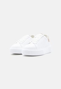 Paire de baskets blanches à plateforme avec semelles épaisses côtelées et accents en daim beige sur le talon, présentées sous un léger angle sur un fond neutre.