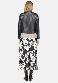 Veste en cuir synthétique noire avec un empiècement au dos, associée à une longue jupe florale noire et blanche. Le modèle porte des bottes noires jusqu'au genou.