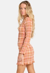 Robe mini froncée en doux motif à carreaux pastel orange et rose. Manches longues et détail à volants au niveau de l'ourlet, fabriquée en tissu texturé léger.
