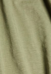 Tissu vert olive avec une surface lisse et légèrement texturée, présentant des lignes horizontales subtiles. Le matériau semble léger et flexible.