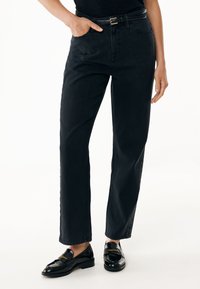 Jeans de mezclilla negra de talle alto con pierna recta, que cuentan con bolsillos delanteros y detalles de botones laterales. Combinados con mocasines negros.