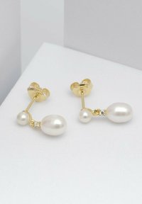 Ohrringe in Goldfarbe mit zwei weißen Perlen in ovaler Form, eine größere mit einem kleinen klaren Edelsteinelement und eine kleinere, verbunden durch einen goldenen Ring.