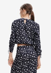 Top nero con stampa floreale, maniche lunghe, tessuto testurizzato e dettaglio a chiave sul retro. Presenta accenti arricciati sulle maniche e in vita.