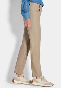 Beige rechte broek met zijzakken, gecombineerd met lichtgekleurde sneakers met suede accenten en veters, op een neutrale achtergrond.