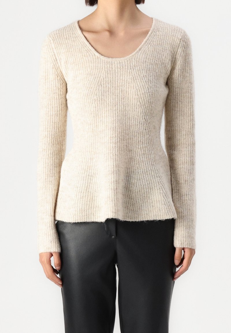 Beżowy prążkowany sweter z dzianiny o okrągłym dekolcie, długich rękawach i lekko rozkloszowanym dole. Połączony z czarnymi skórzanymi spodniami.