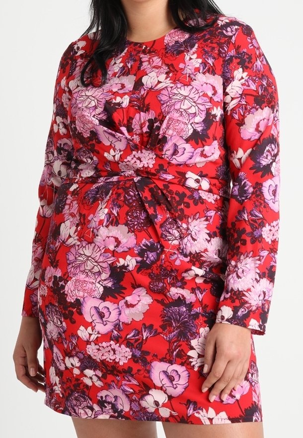 Robe fleurie rouge avec manches longues et détail noué à la taille. Le tissu présente un mélange de motifs floraux roses, violets et noirs.