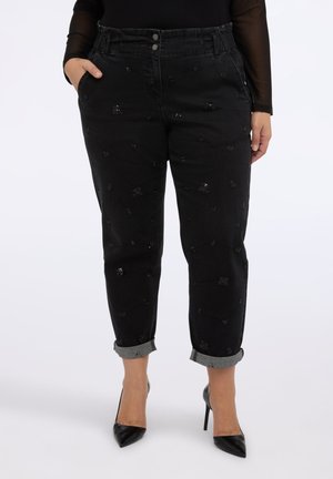 Vaqueros negros de cintura alta con pequeños patrones florales de lentejuelas negras, puños doblados, usados con tacones altos negros puntiagudos y una blusa negra transparente.