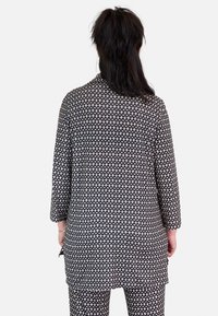 Camisa de manga larga de patrón en blanco y negro con estampado geométrico, de corte ligeramente holgado y con aberturas laterales, vista desde atrás.